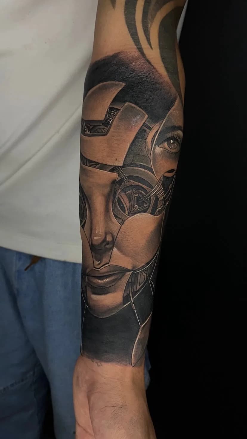Tatuagem biomecânica com rosto feminino em preto e cinza no antebraço