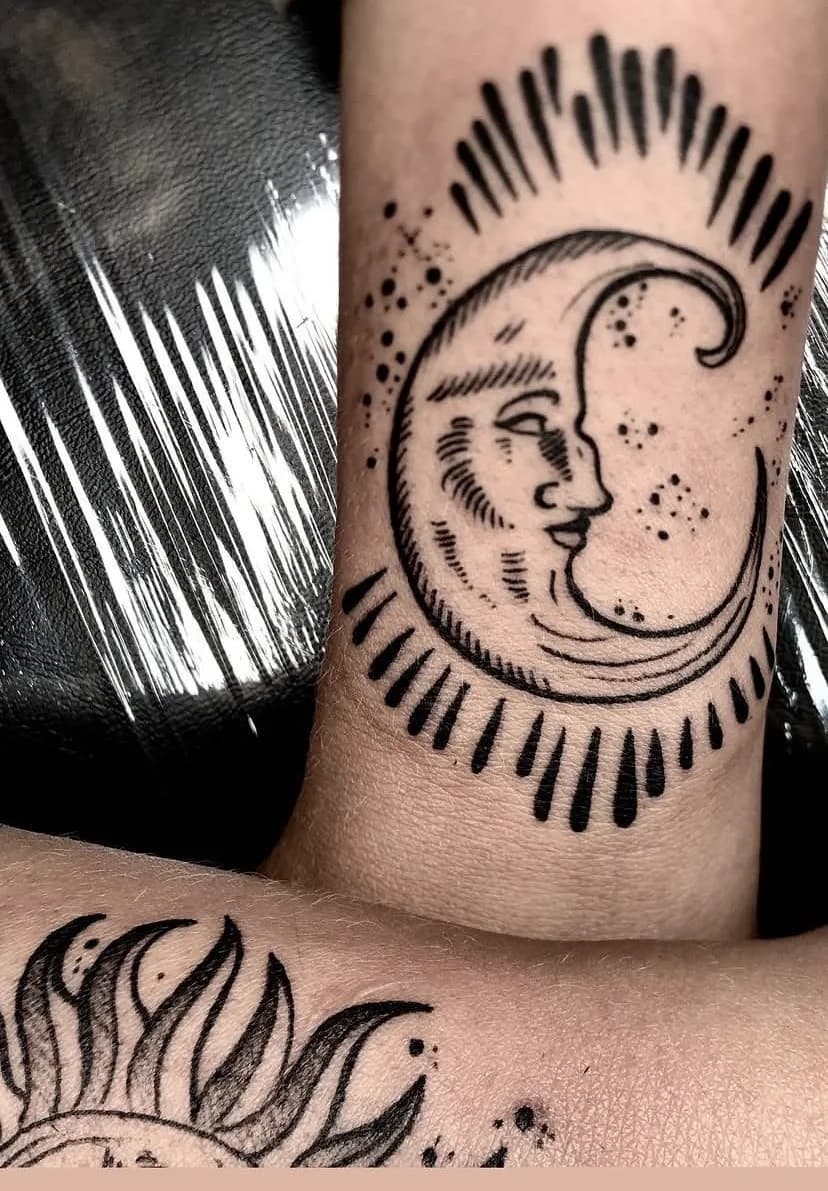 Tatuagem de lua crescente com rosto em preto e cinza no antebraço